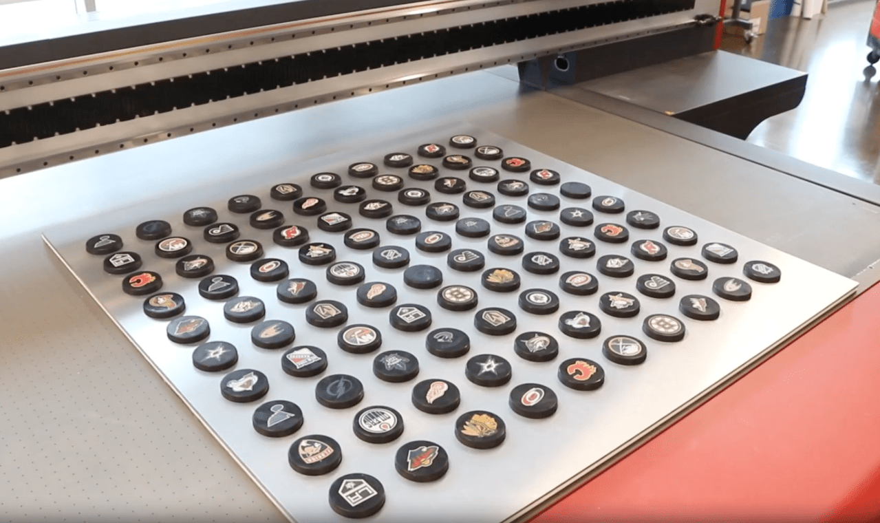 Various logos printed on hockey pucks using a jig.